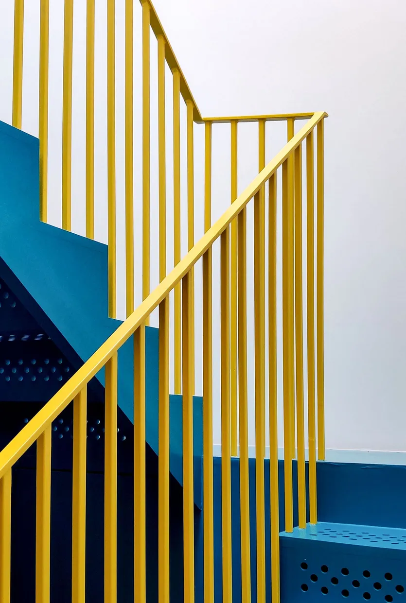 A vibrant yellow stair railing against a minimalist blue and white background.