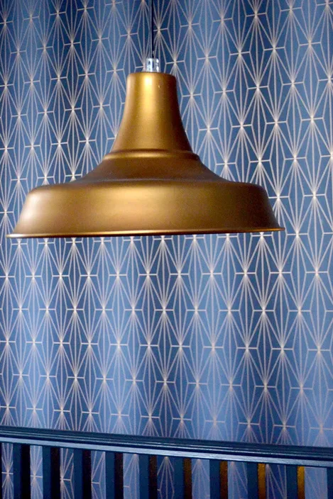 Brass pendant light with the background of blue walls, and railing. The walls have geometrical pattern.