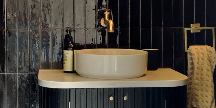 Modern bathroom vanity with a vessel sink, brass faucet, and black wall tiles.