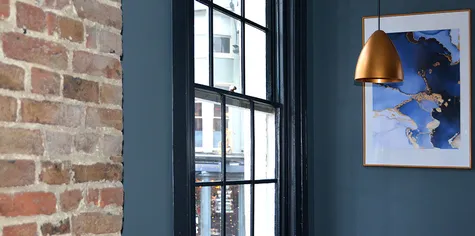 Interior space of a restaurant bistro showing grey/blue walls followed by a natural brick wall element. There are golden elements that lighten the atmospher ein the space and make it seem more luxurious.