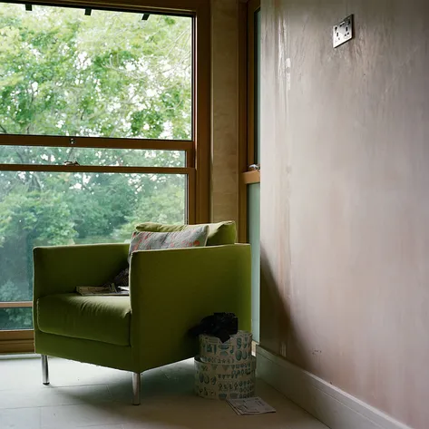 A cozy green armchair placed by a large window, with soft natural light illuminating the room and a view of trees outside.