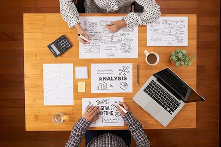 Two People sitting in front of the desk with sheets of paper suggesting in-depth business analysis