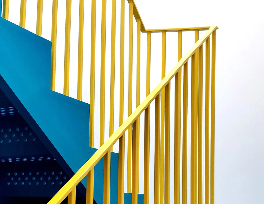 A vibrant yellow stair railing against a minimalist blue and white background.